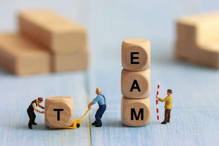 Group of miniature people assemble wooden cube, team support and help concept. Business teamwork concept.の写真素材