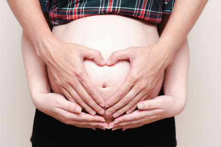 A pregnant woman and her husband makes a heart-shaped hand to present love for the baby in her belly.の写真素材