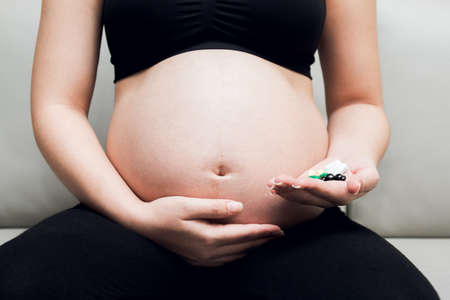 Pregnancy woman sitting on sofa and hand holding medicine pills.の写真素材