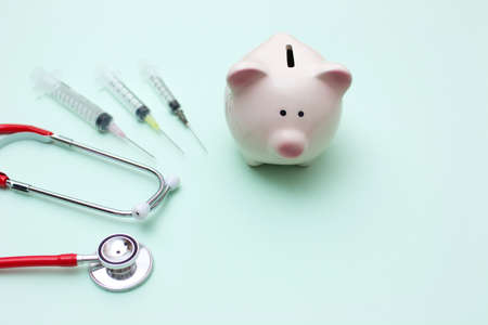 Pink piggy bank with stethoscope and syringe on green backgroundの写真素材