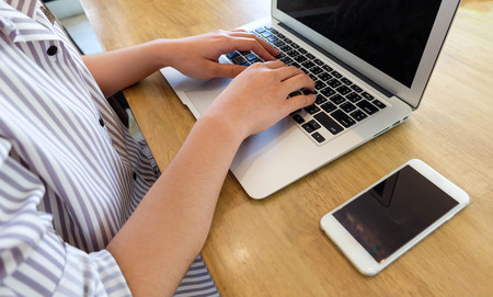 Woman office worker is typing keyboard of laptop with mobile phone, business or learning conceptの写真素材