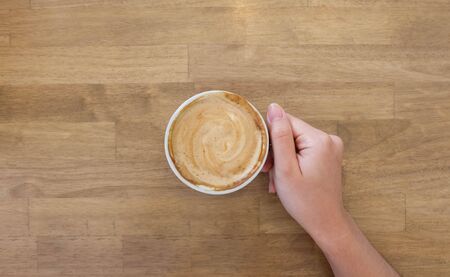 Woman hands holding a cup of coffee with latte art in a brown cup on wooden table background