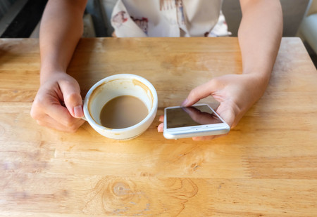 Woman using mobile phone and drink a cup of coffee, close up