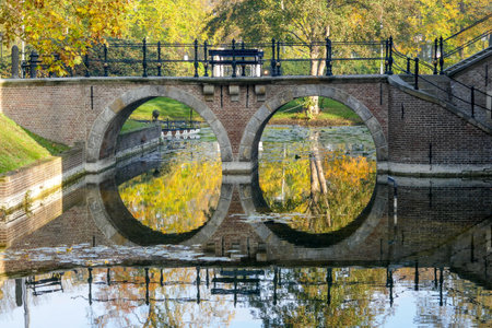 Public park in autumn with an arched castle bridge, reflecting in the moat water. Shot in Ruurlo,...