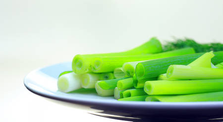 sliced green onions and dill close-up. On the plate are onions and the bunch of greens in the backgroundの写真素材