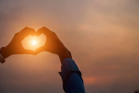 Hands forming a heart shape with sunset silhouetteの写真素材