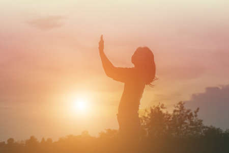 Silhouette of woman praying over beautiful sky backgroundの写真素材