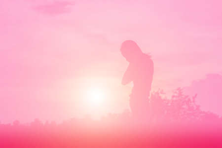 Silhouette of woman praying over beautiful sky backgroundの写真素材