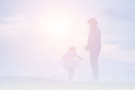 Silhouette of Mother and Baby Daughter Running and Dancing at Sunsetの写真素材