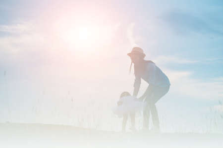 Silhouette of Mother and Baby Daughter Running and Dancing at Sunsetの写真素材