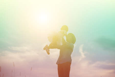 Silhouette of Mother and Baby Daughter Running and Dancing at Sunsetの写真素材