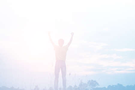 Silhouette of a man raising his hands looking at the sunset at the coastline. Grandness conceptの写真素材