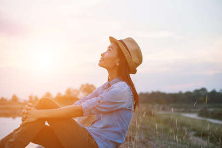An adult woman wearing a hat sitting by the coastline during sunset