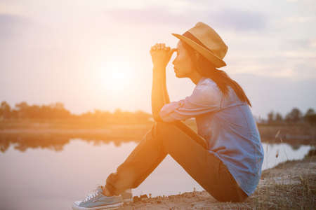 An adult woman wearing a hat sitting by the coastline during sunset