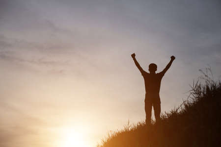 An adult man raising his arms in joyous looking at the coastline during sunsetの写真素材