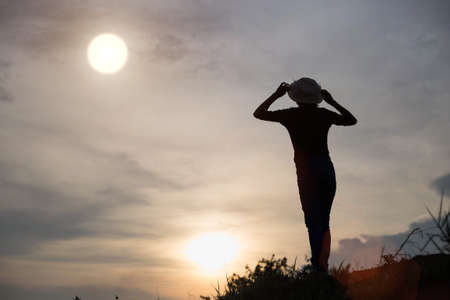 A lonely adult woman looking at the coastline during sunsetの写真素材
