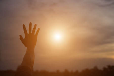 Hand pointing up in the air behind a sunsetの写真素材