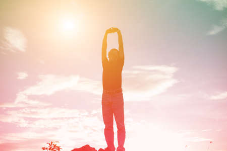 An adult man raising his arms at the coastline during sunsetの写真素材