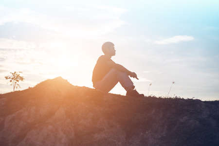 An adult man sitting alone at the coastline during sunsetの写真素材