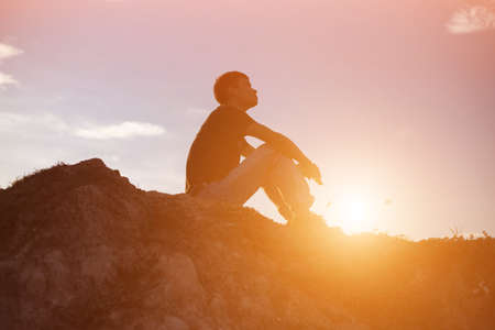 An adult man sitting alone at the coastline during sunsetの写真素材