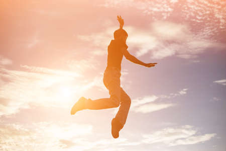 An adult man jumping at the coastline during sunset
