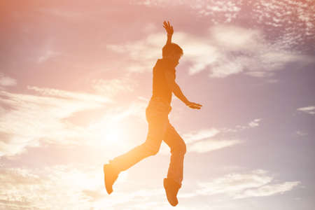 An adult man jumping at the coastline during sunsetの写真素材