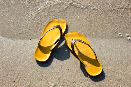 Slipper on the beach, sandals on the beach. Flipflops on a sandy ocean beach - summer vacation concept. Beach summer casual shoes. Copy spaceの写真素材