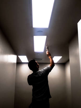 The black silhouette of the technician working on the ceiling, Workers are painting bright ceilings on large ceilings, Silhouette technician who painted the ceiling painted with fluorescent lightingの写真素材