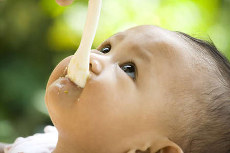7 months baby looking up while having a meal with spoon in mouthの写真素材