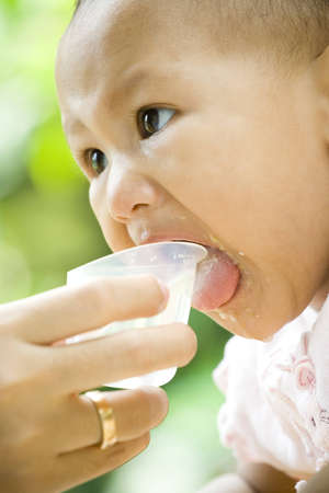 7 months baby open mouth while having a drink on meal time. mother hand holding a cup of waterの写真素材