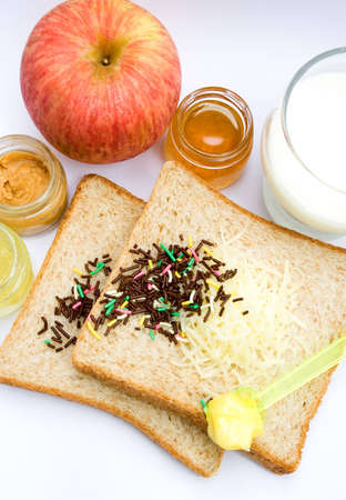 meal ingredient for healthy & easy breakfast: wheat bread, fruit jam, chocolate sprinkles, a glass of milk and appleの写真素材