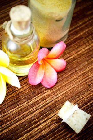 bottles of body oil and scrub powder as spa items with tropical flowers. shallow deep of field with selective focus on flower in frontの写真素材