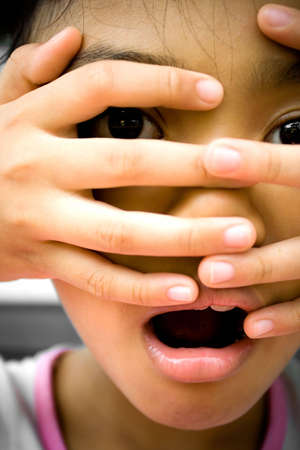 little girl looks surprising and terrified onto something she saw. putting her fingers over her face.の写真素材