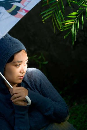 portrait of asian woman on her sweater and holding an umbrella on a cold and rainy night. seems to worry of something and feeling insecure of her current circumstances. の写真素材