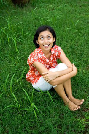 happy asian woman sitting on green grass and looking up to the sky, cheering a day in nature. の写真素材