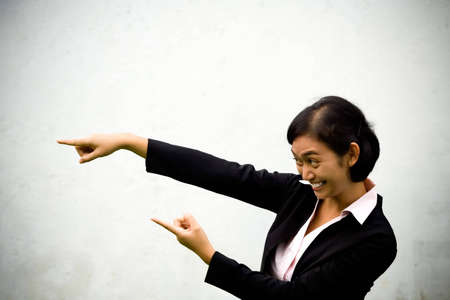 cheerful asian business woman pointing at someone (her colleague) or something that just emerge, seems to happy as she finally found what she has been looking for. の写真素材