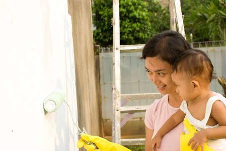 conceptual portrait of multitasking mother. asian mother sitting and educating her girl during painting job.の写真素材