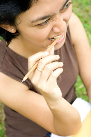 conceptual portrait of a pretty asian woman making face and biting a pencil, seems to have some deep thought of something.の写真素材