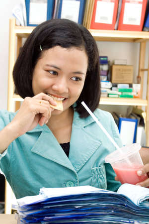 asian female employee eating snack and drinking while at workの写真素材
