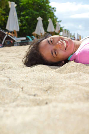 Ethnic young woman happy lie down on tropical beach sandの写真素材