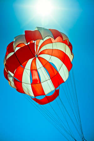 white and red parachute in the blue sky wth bright sun behindの写真素材