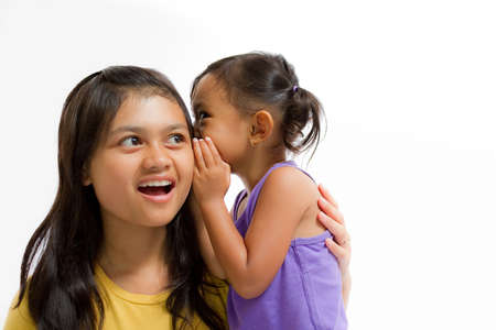 Asian Little Girl Whispering Something to Teen Sister Isolated on Whiteの写真素材