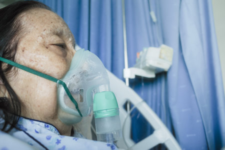 Southeast Asian female senior patient being treatment in hospital using nebulizerの写真素材