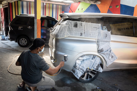 Southeast Asian adult male worker repainting silver car. Car body covered with used newspaperの写真素材