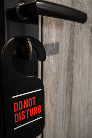 Black do not disturb sign with red text hanging on door key at hotel guest room