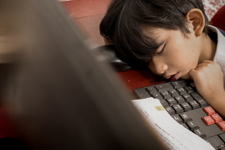 Asian boy fallen asleep in front of his computer during online school from homeの写真素材