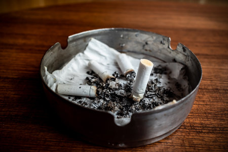 Burnt cigarettes in an ashtray on a wooden table with wet tissue insideの写真素材