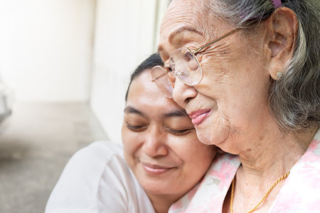 An Asian old mother smiling and happy being hugged by her daughterの写真素材