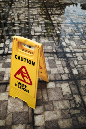 Two-Sided Yellow Wet Floor Warning Sign Board Placed Standing on Dirty Mossy Wet and Flooded Outdoor Floorの写真素材