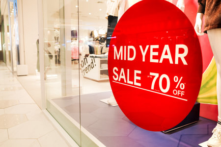 Red 70 Percent Mid Year Sale Sign Sticker on Display Window Near Fashion Clothing Store Entrance in...